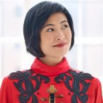 Jennifer Koh, holding her violin, smiles as if inspired by a musical idea.